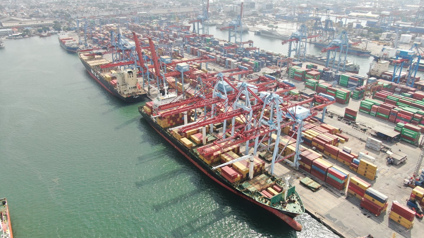 Aerial view of busy industrial port with cargo ships and cranes.