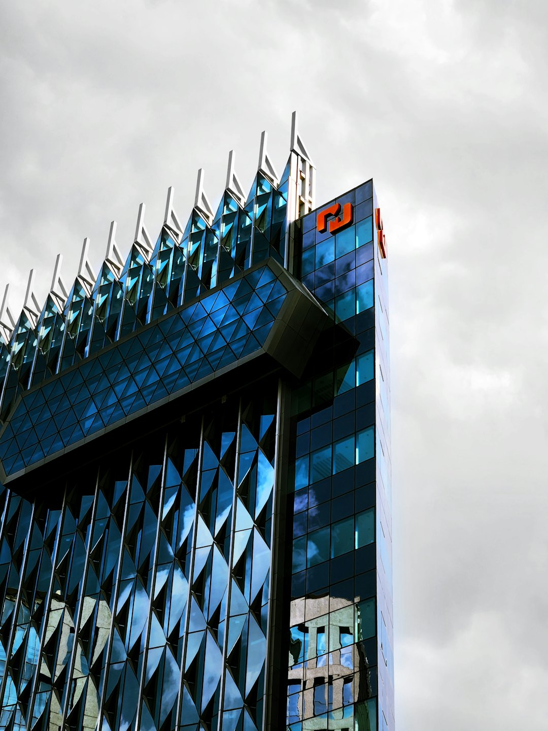 Modern blue glass office building with geometric patterns and orange logo.